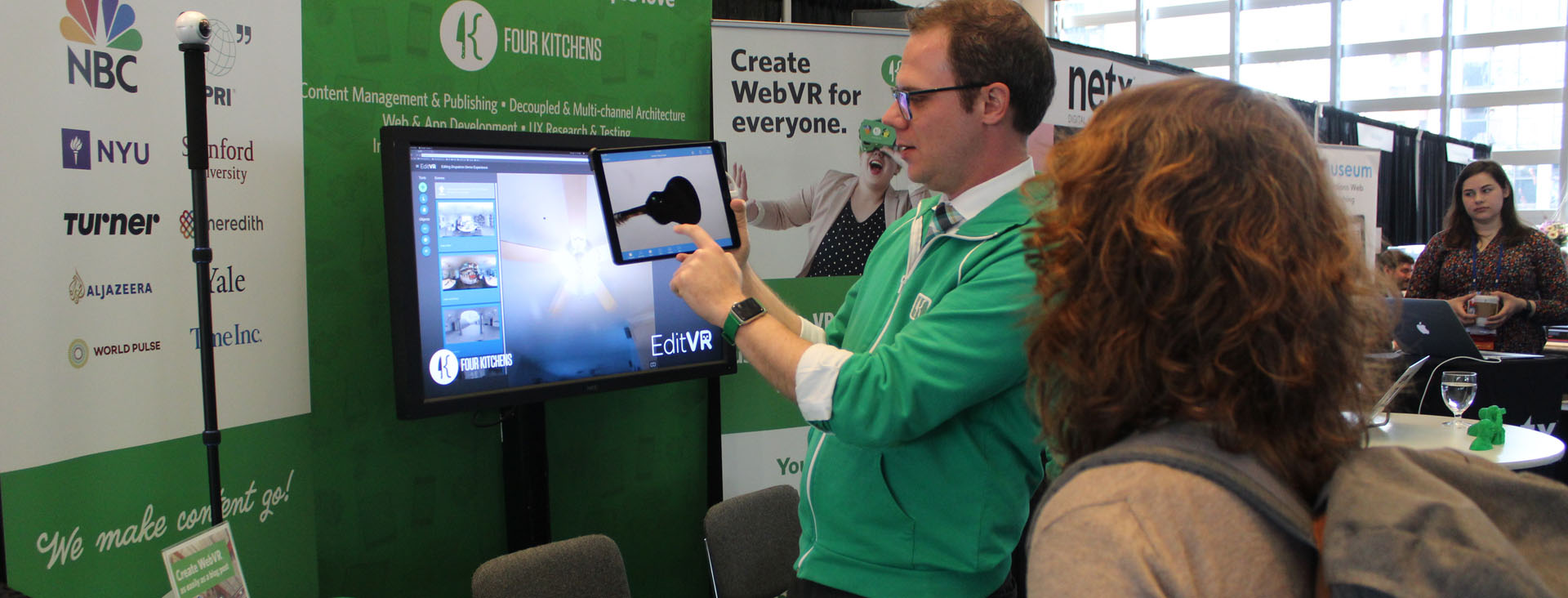 A man in a green sweater does a demonstration on an iPad for a woman in the Vendor Hall at MW18.